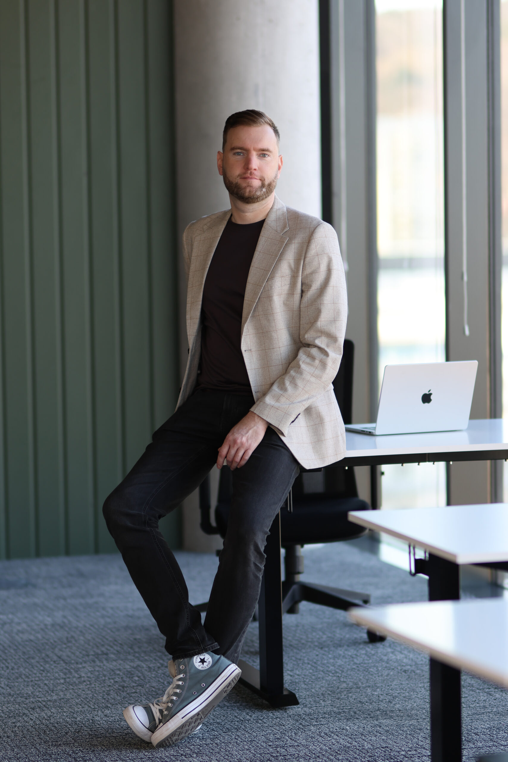 Man sitting on desk near laptop in office.