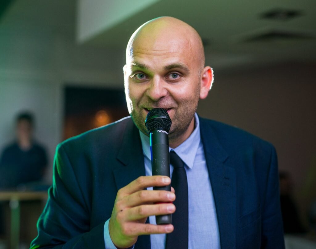 Man in suit speaking into microphone at event.