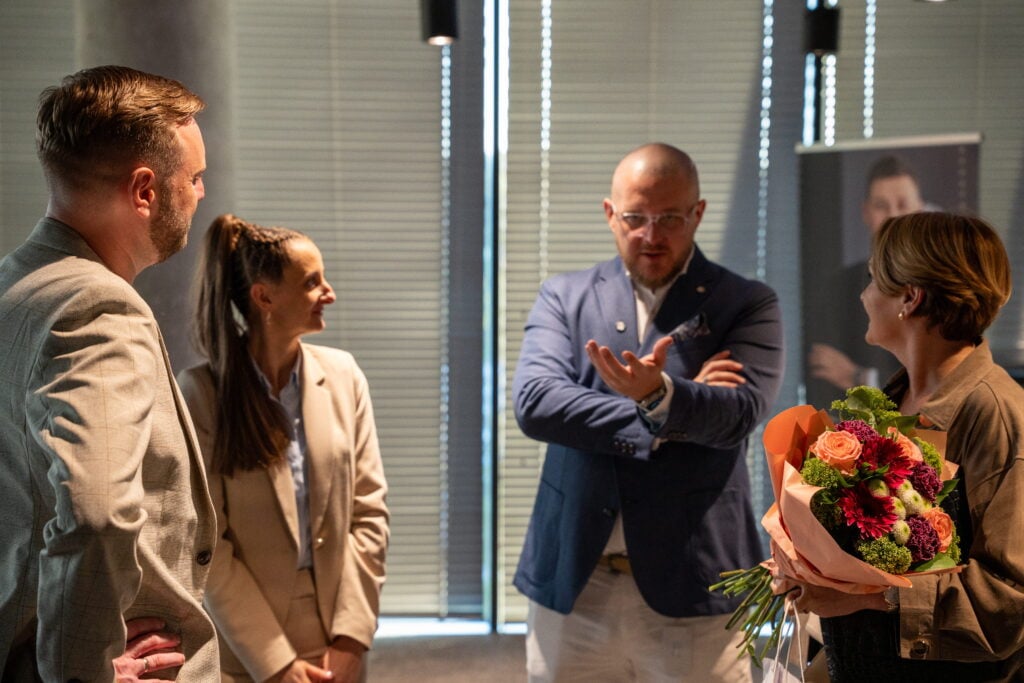Four people chatting with bouquet indoors.