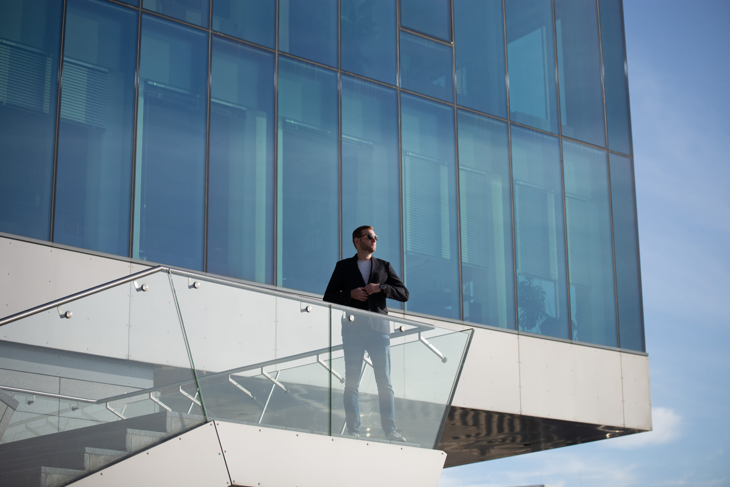 Man standing on modern building glass balcony.