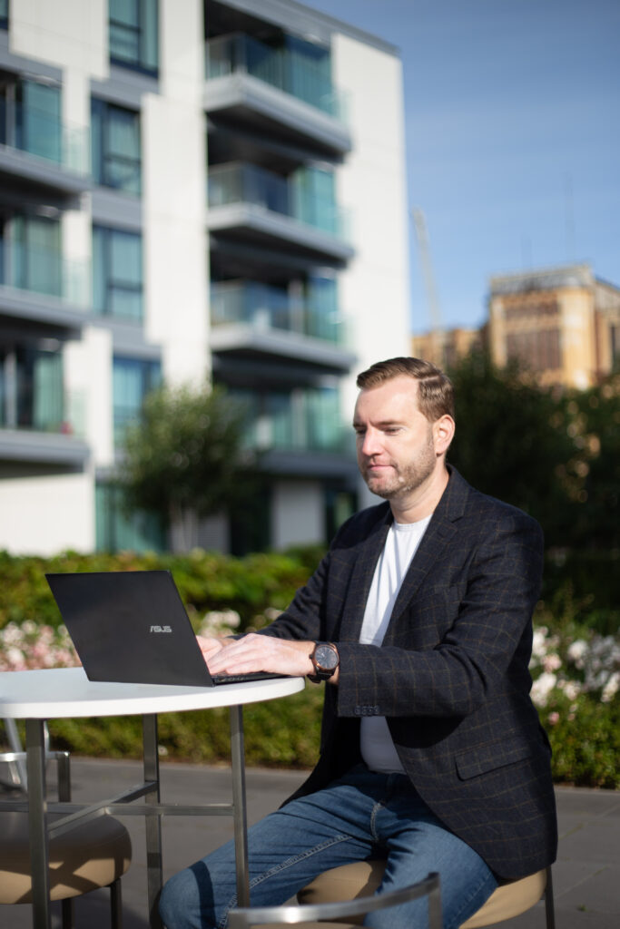 Man using laptop outdoors by modern buildings.