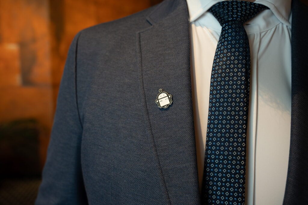 Man in suit with robot badge and patterned tie.
