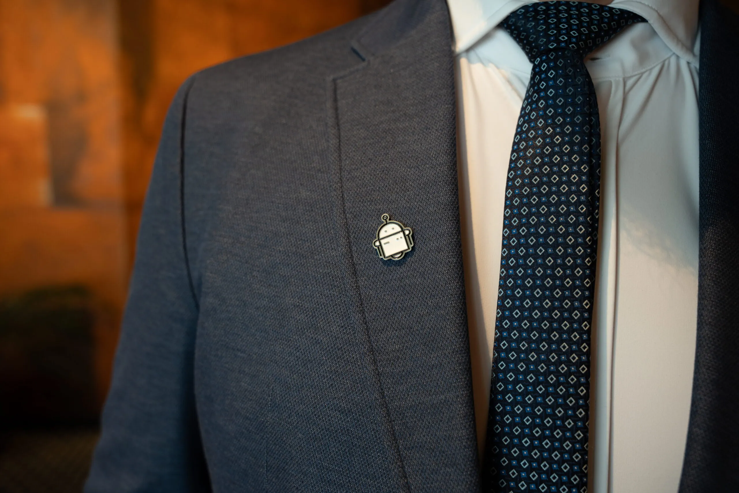 Man in suit with robot badge and patterned tie.