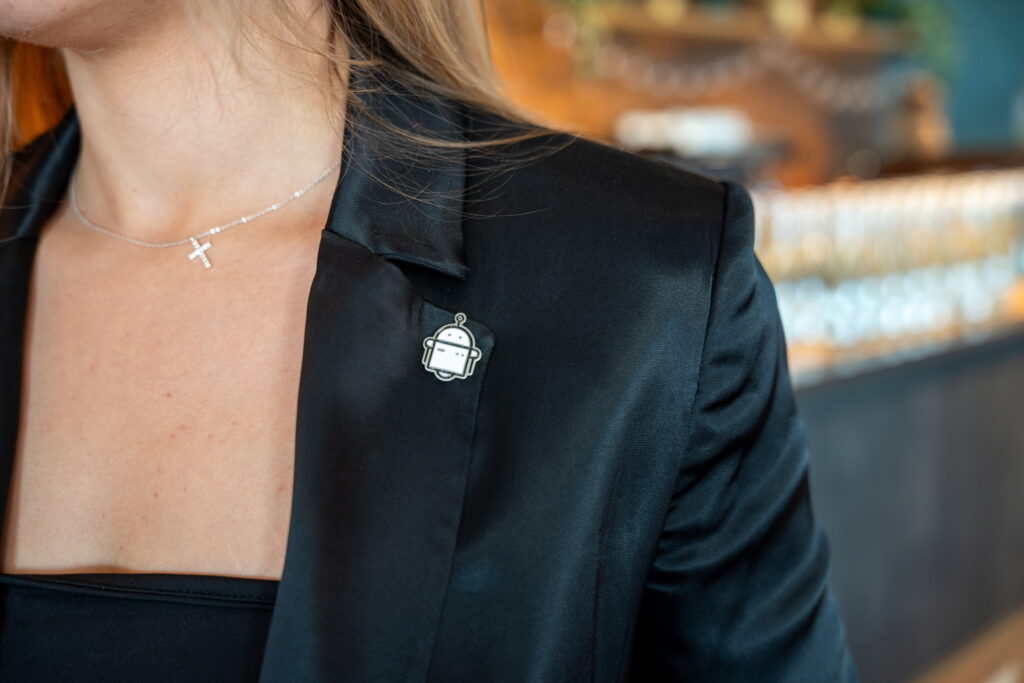 Woman wears cross necklace and robot pin on jacket.