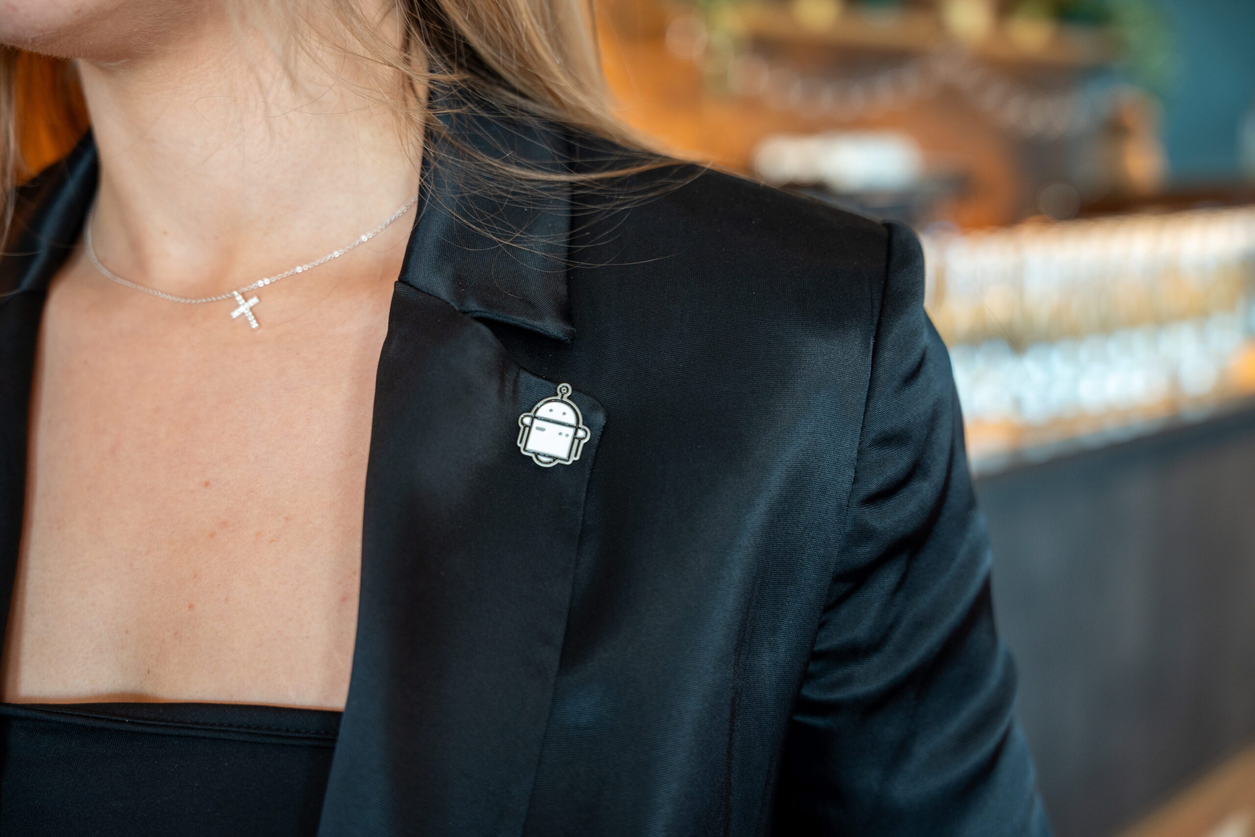 Woman wears cross necklace and robot pin on jacket.