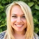 Smiling person with blonde hair and green leaves background.