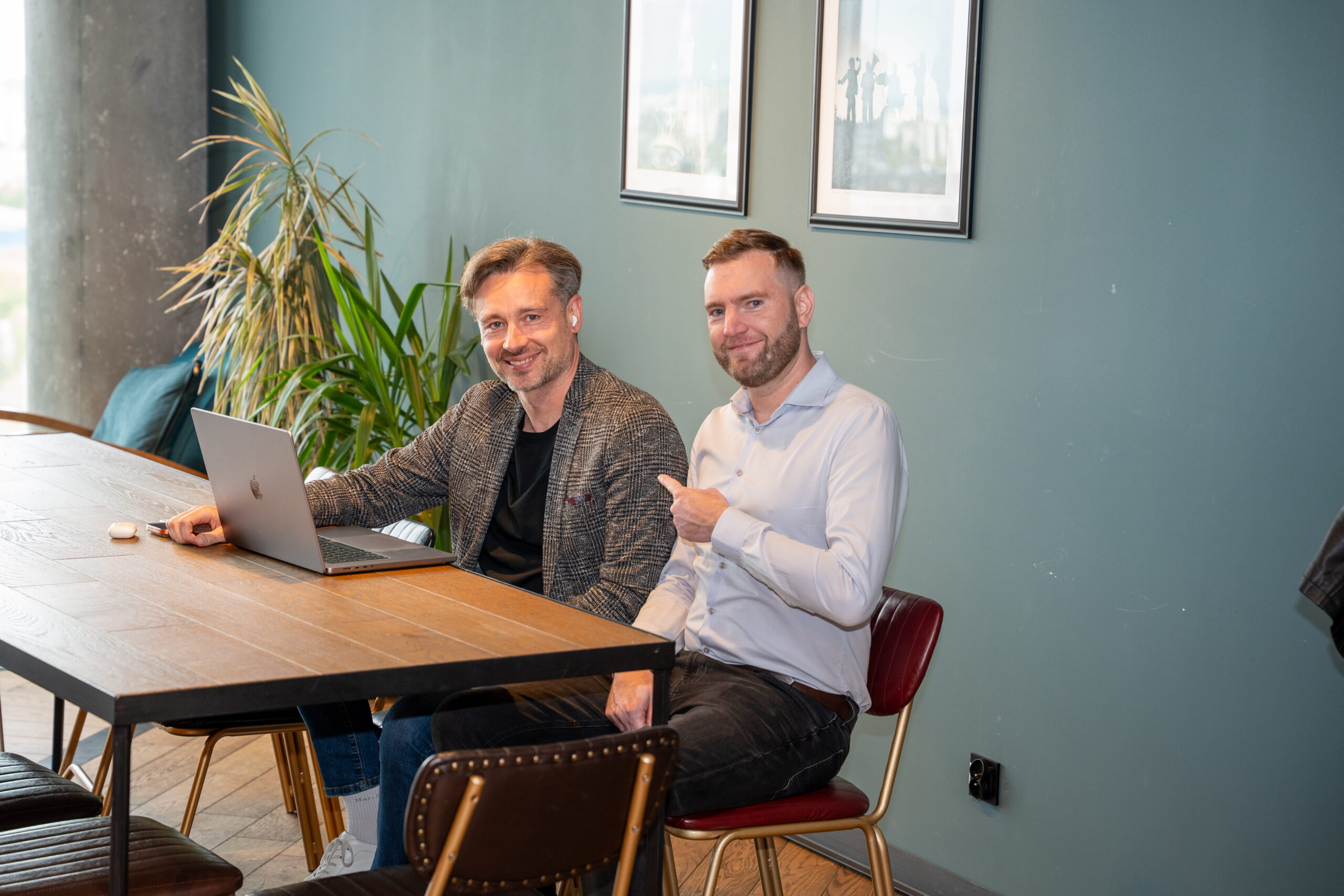Two men smiling at office table with laptop.